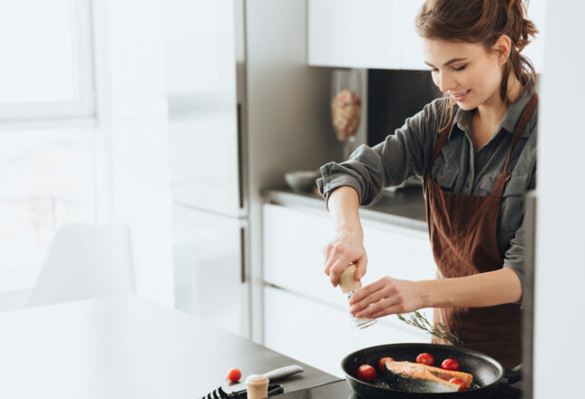 Pretty lady standing in kitchen while cooking fish